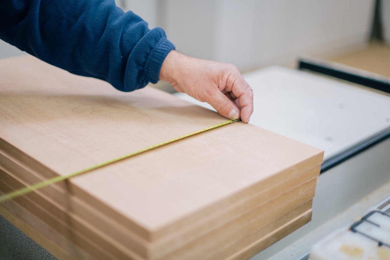 Close-up of a carpenters hand using a tape measure to measure wooden planks indoors.